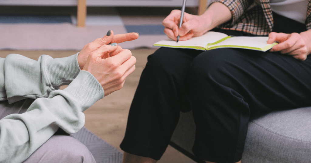 Two people sitting down and one of them writing in a journal