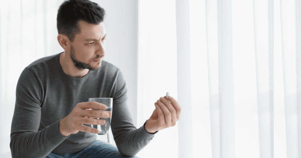 Man holding a pill and a glass of water