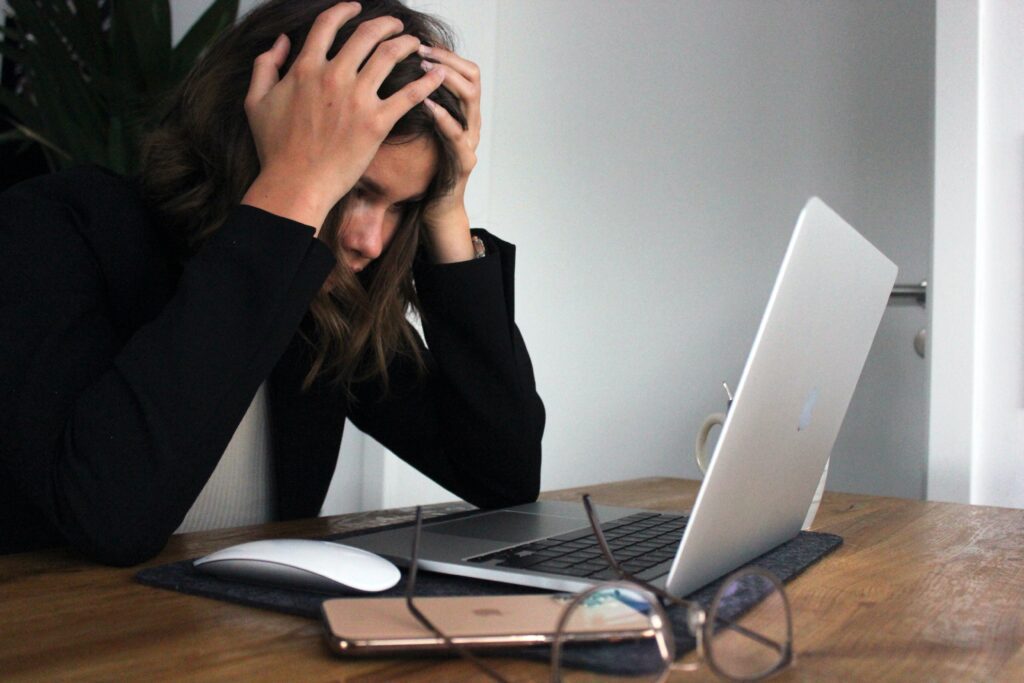 Woman sitting at a desk in front of a laptop with her head in her hands 