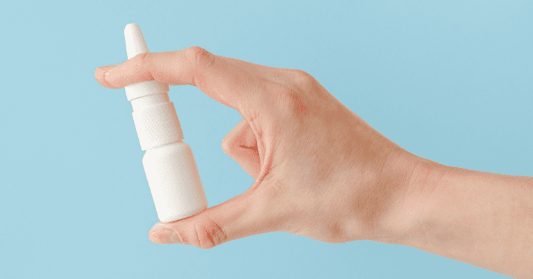 A hand holding a bottle of nasal spray
