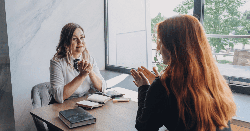 Two people sitting at a desk across from each talking