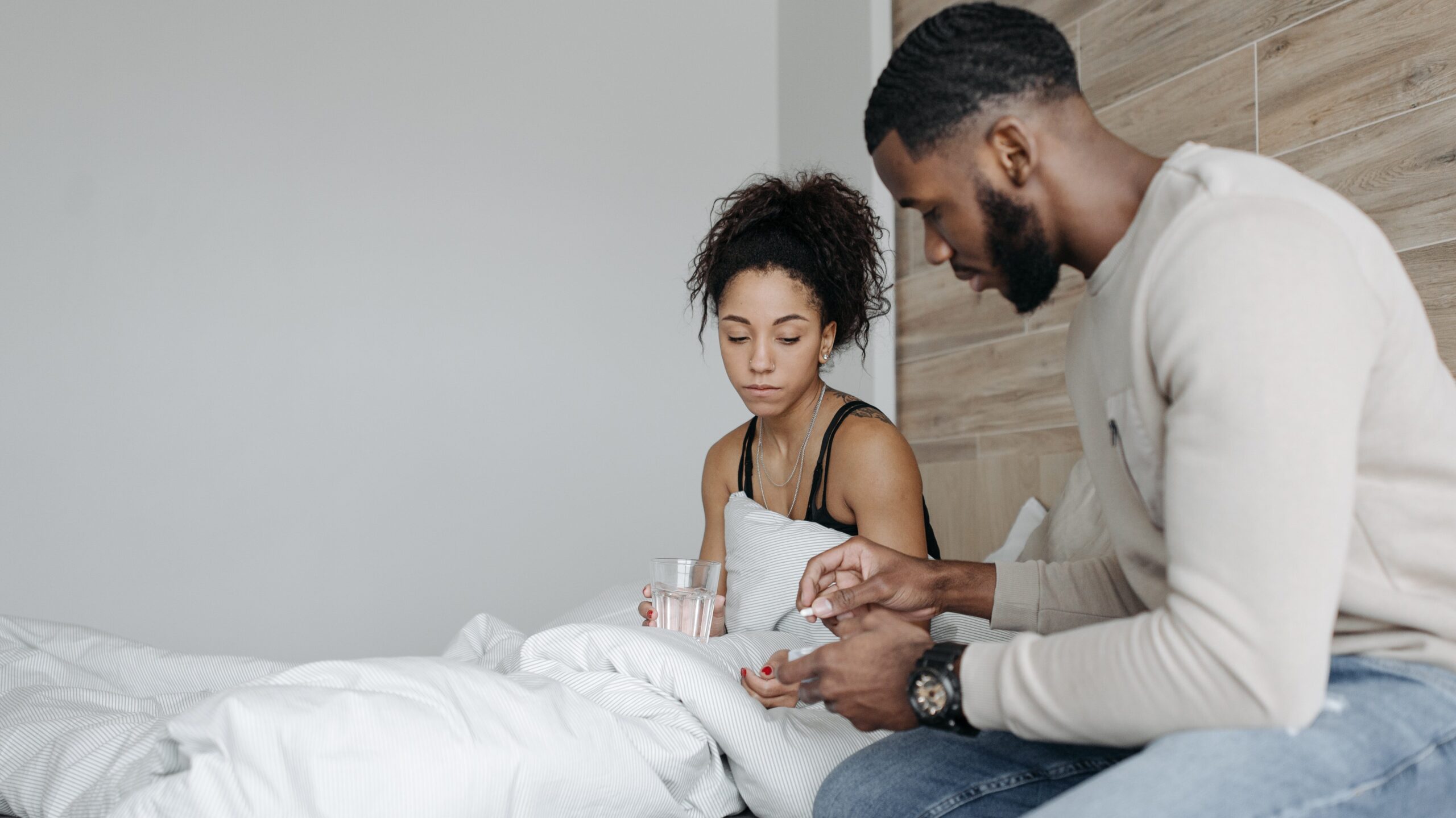Man giving a woman pills while sitting in bed