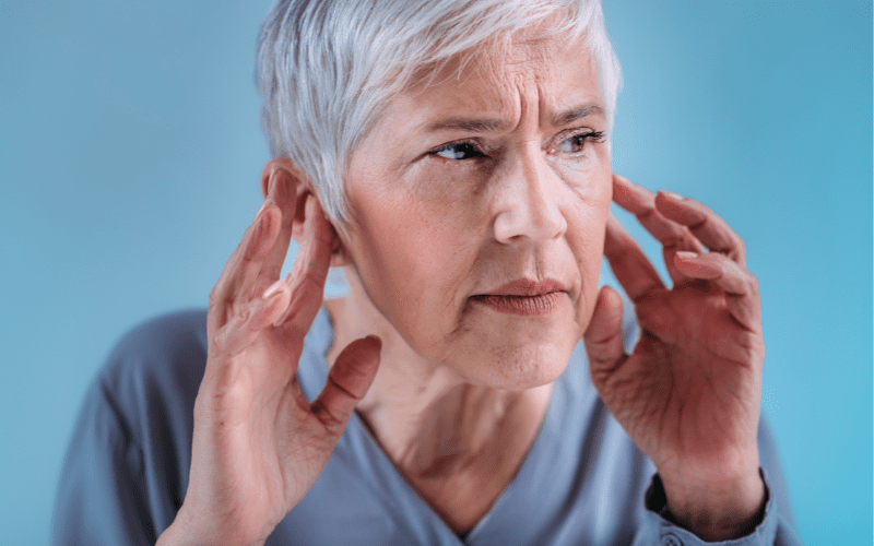 Older woman with hearing loss holding her ears to hear better