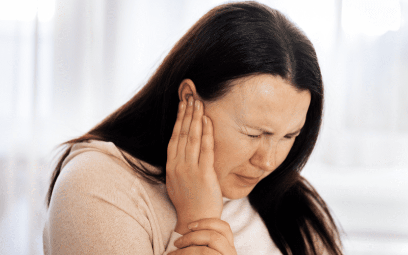 Woman with tinnitus holding her ear in pain
